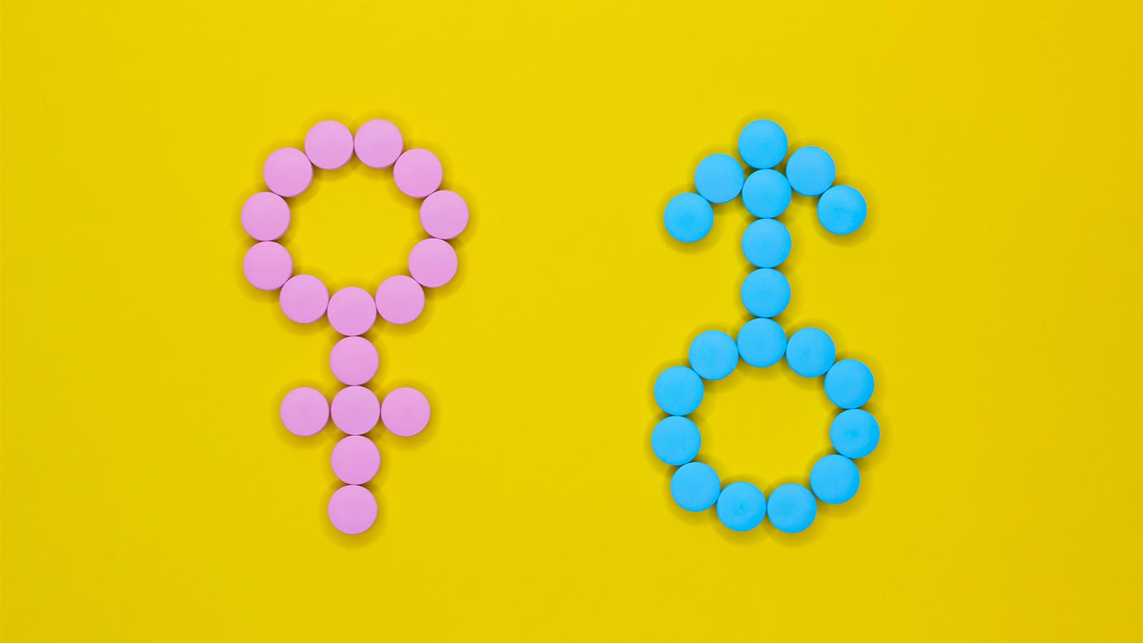 A photo of pink pills arranged to form the female symbol, and blue pills arranged to form the male symbol.